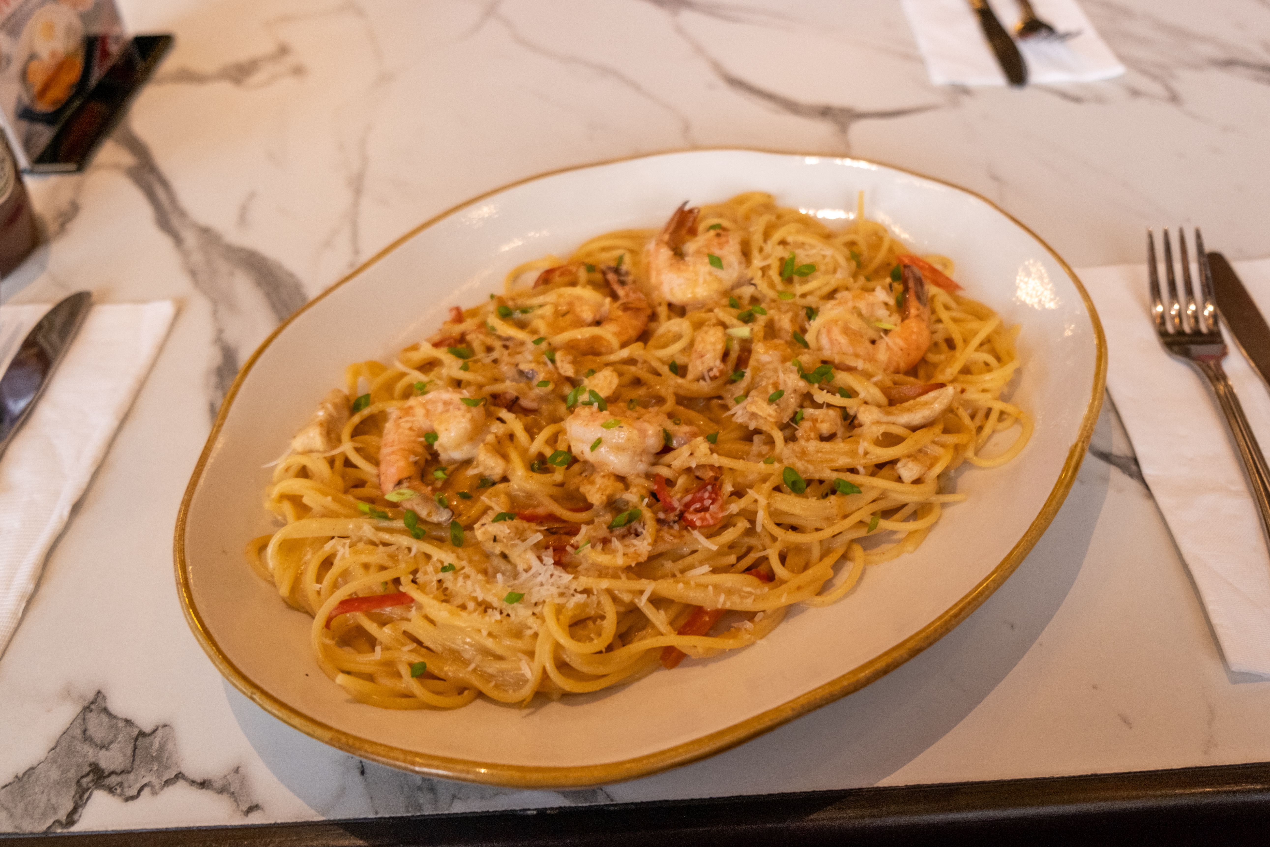 Oval platter of shrimp linguine tossed with herbs and tomato on a marble tabletop