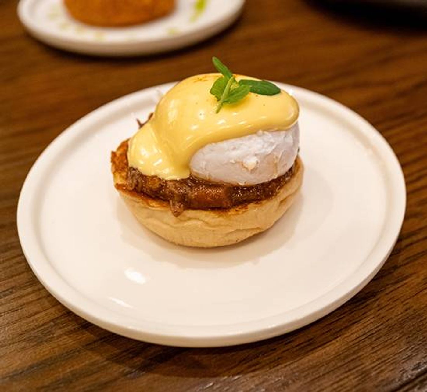 Braised lamb benedict: poached egg and Hollandaise over meat on an English muffin, herb sprig on top
