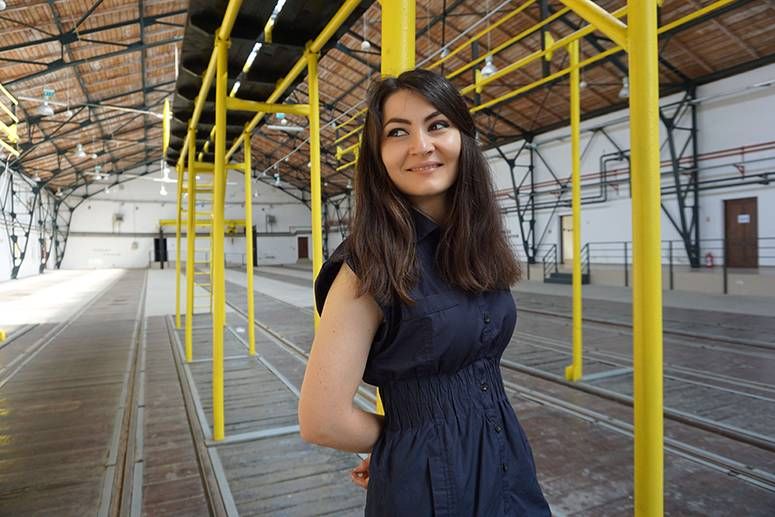 Andreea Medar smiles over her shoulder in a hall framed by yellow scaffolding beams