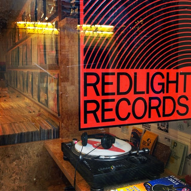 Turntable and headphones in a shop window behind a red and black Redlight Records sticker