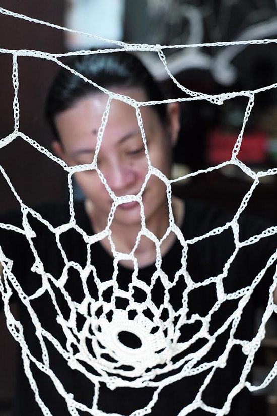 A white crocheted web in sharp focus, artist Aze Ong in black softly blurred behind it