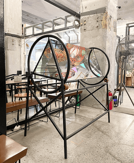 Marco Ortiga’s Kaleidoscope 01, twin black steel hoops framing a mirrored kaleidoscope chamber inside an industrial concrete cafe