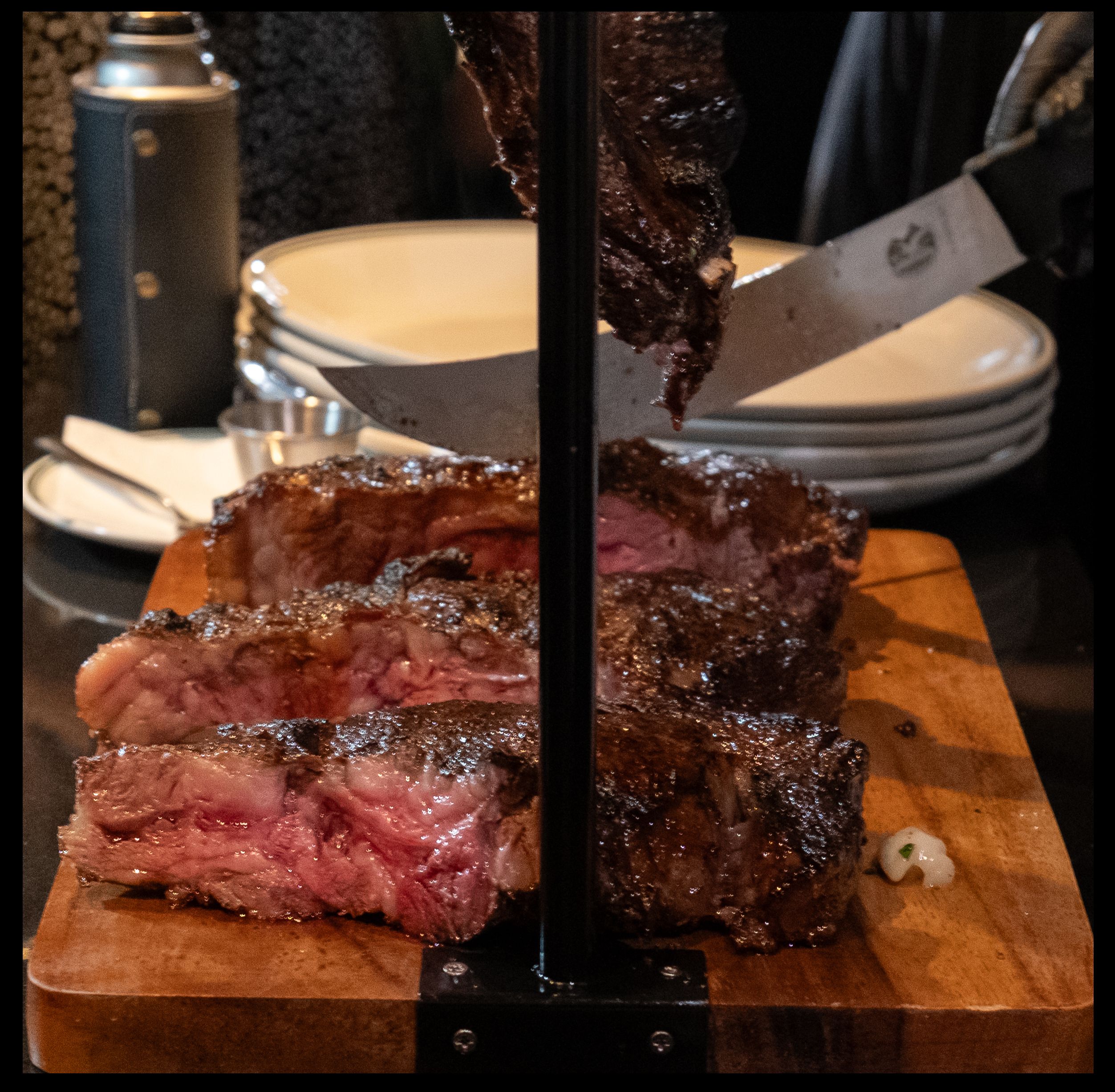 A dry-aged tomahawk steak carved tableside into rosy medium-rare slabs on a vertical stand at Smith & Wollensky