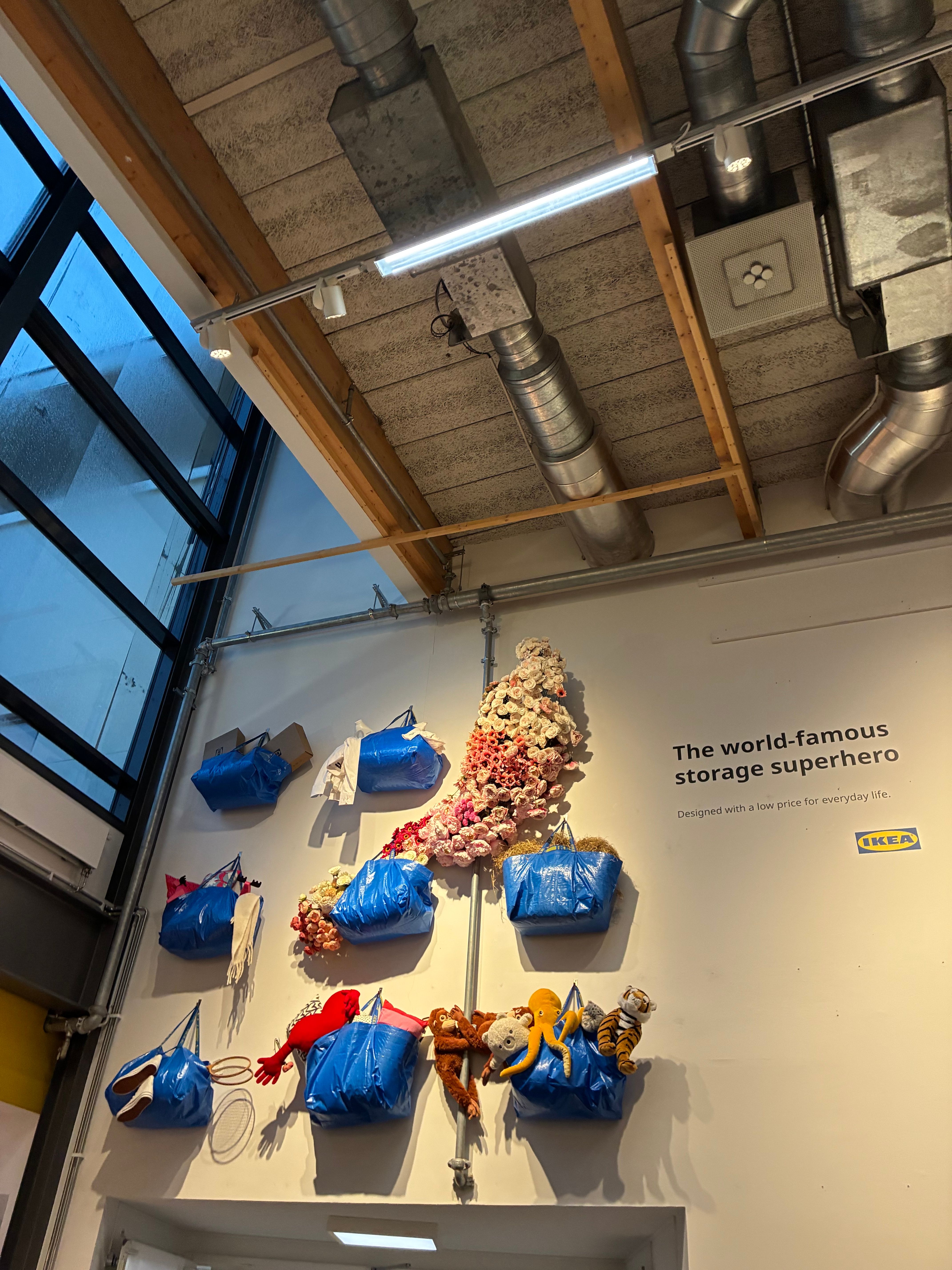 Blue IKEA carrier bags mounted on a wall spilling flowers and plush toys under the words The world-famous storage superhero