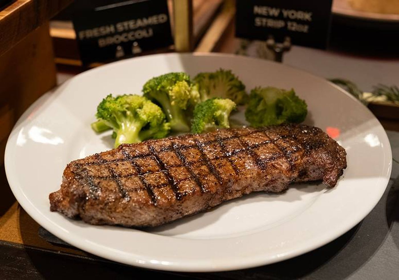 Fire-grilled New York strip with crosshatch char beside steamed broccoli on a white plate