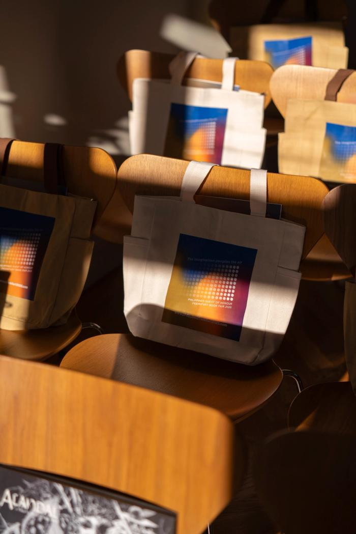 Canvas tote bags printed with a glowing gradient design resting on rows of curved wooden chairs