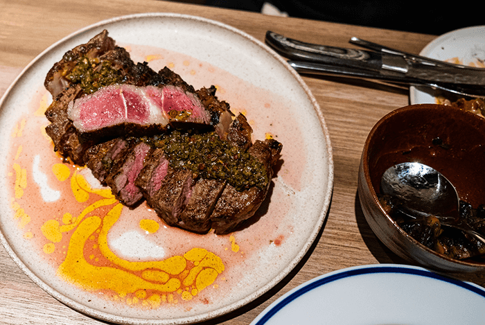 Slices of medium rare ribeye steak under a green herb sauce on a speckled ceramic plate