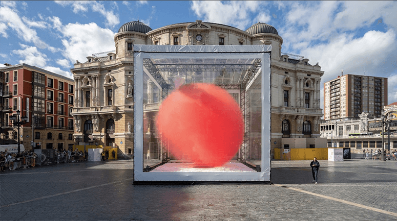 A ten-meter red globe tilted inside a scaffolding cube on the plaza of Teatro Arriaga, Bilbao
