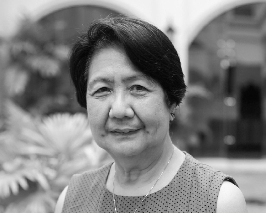 Black-and-white portrait of Fe Prudente, short-haired in a polka-dot top, in a garden courtyard
