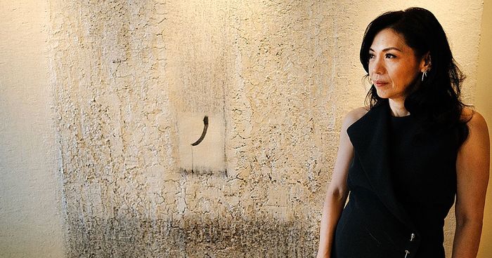 Kaye Tinga, president of the Cultural Center of the Philippines, standing in a black top against a textured wall with a minimalist abstract painting