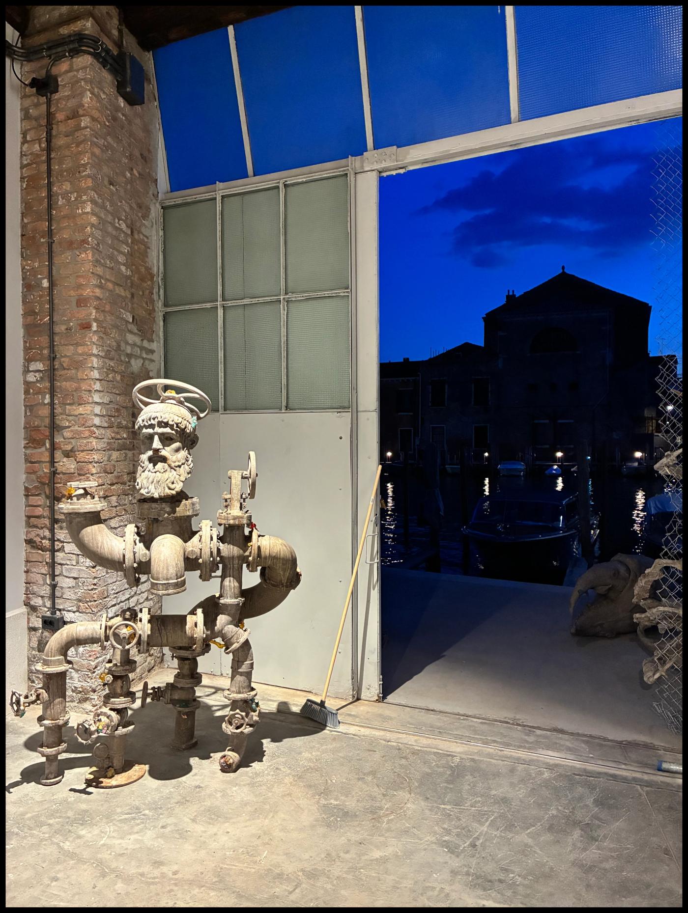 The assemblage figure “Obsolescence,” built of metal, fiberglass-resin and oyster shell, stands in a doorway of the dock warehouse