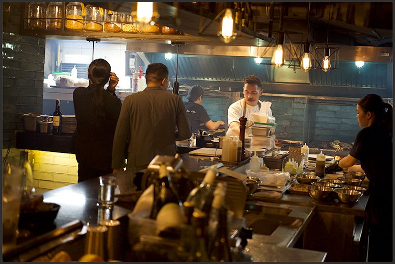 Guests watch chef Josh Boutwood work behind the counter of his dimly lit open kitchen, cluttered with pans, bottles and mixing bowls