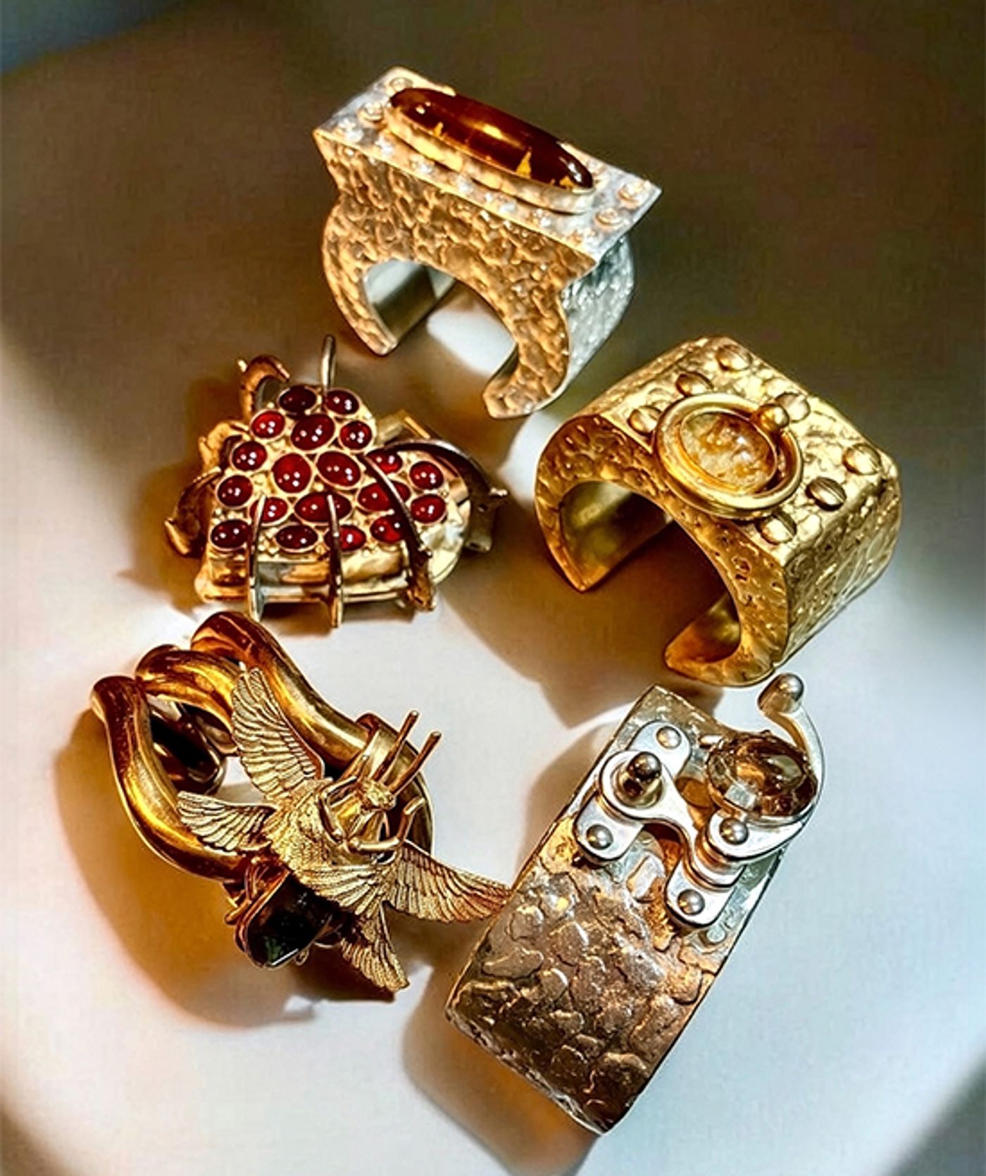 Five sculpted cuffs by Michelline Syjuco in oxidized silver and gold tones, one studded with red cabochons