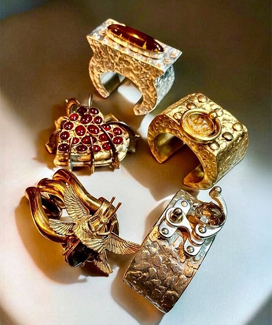Five sculpted cuffs by Michelline Syjuco in oxidized silver and gold tones, one studded with red cabochons