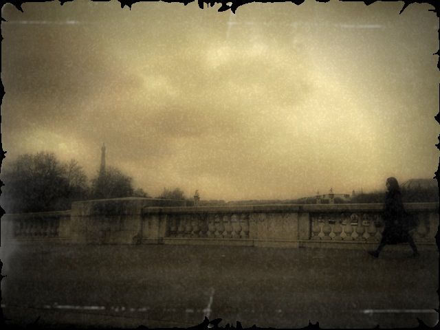 Sepia toned stone bridge balustrade with a lone figure walking, the Eiffel Tower faint in the distance