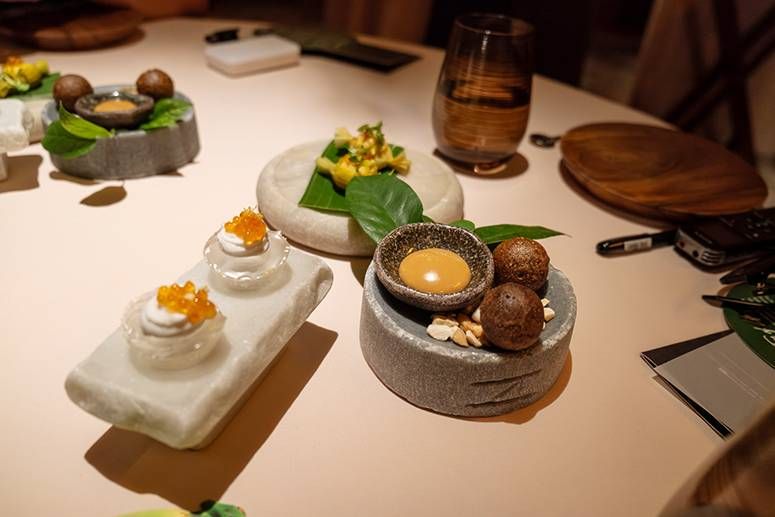Bite-sized coconut snacks with roe-topped cream puffs and kare-kare bonbon spheres on rough stone plates