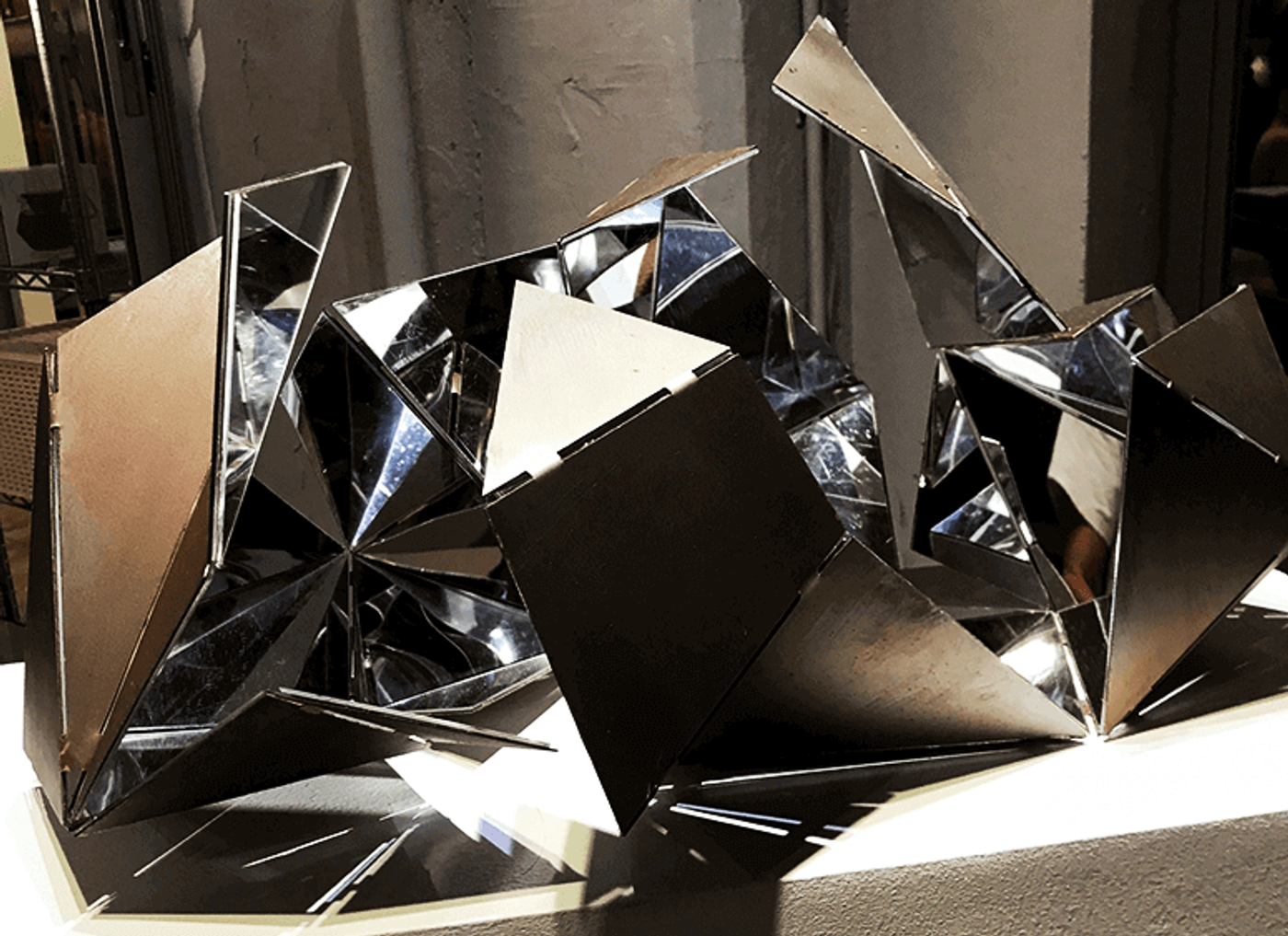 Marco Ortiga’s Deconstructed Kaleidoscope, angular mirror-polished steel planes splayed open like a collapsed kaleidoscope on a lit plinth