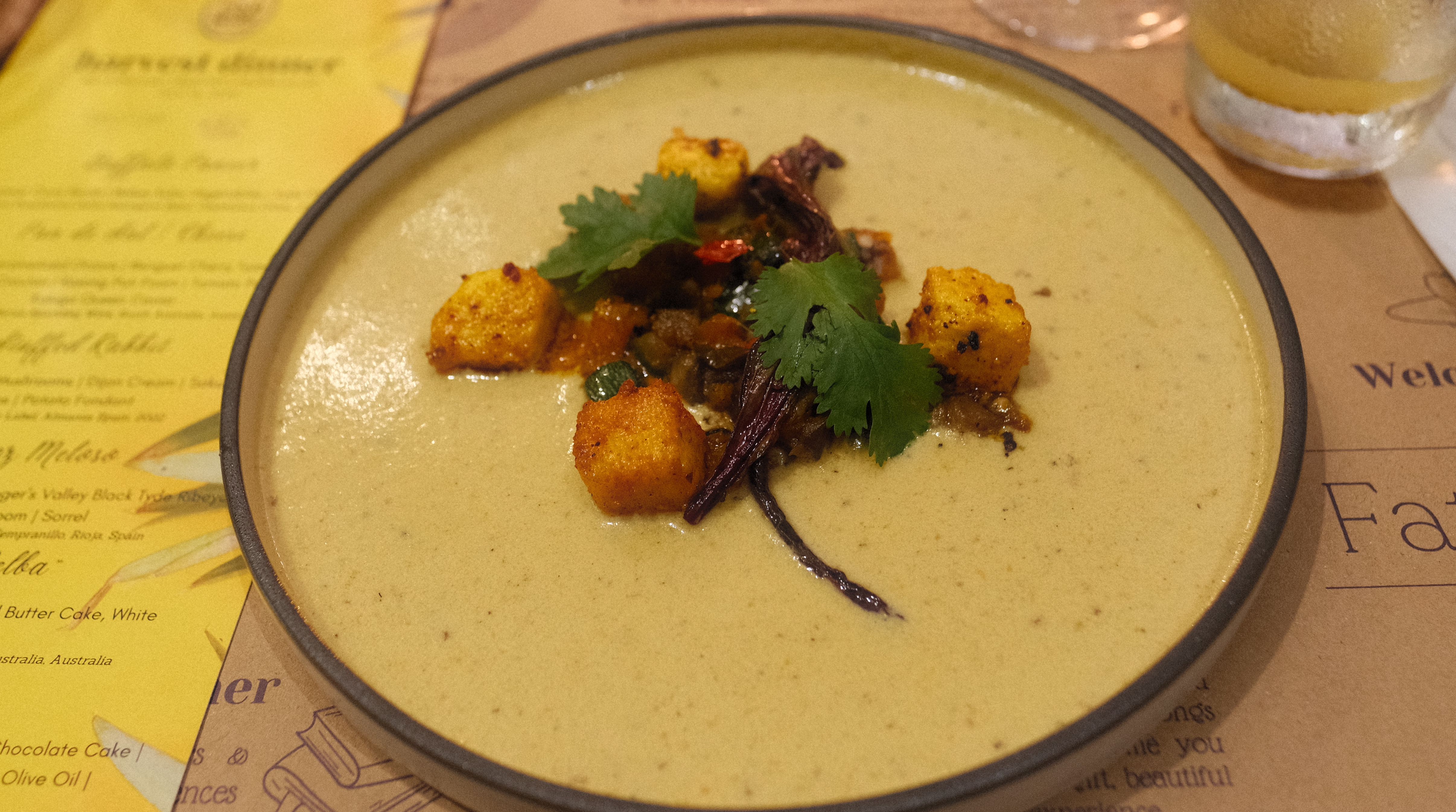 Buffalo paneer: golden fried paneer cubes and herbs over a creamy pale soup in a dark-rimmed bowl