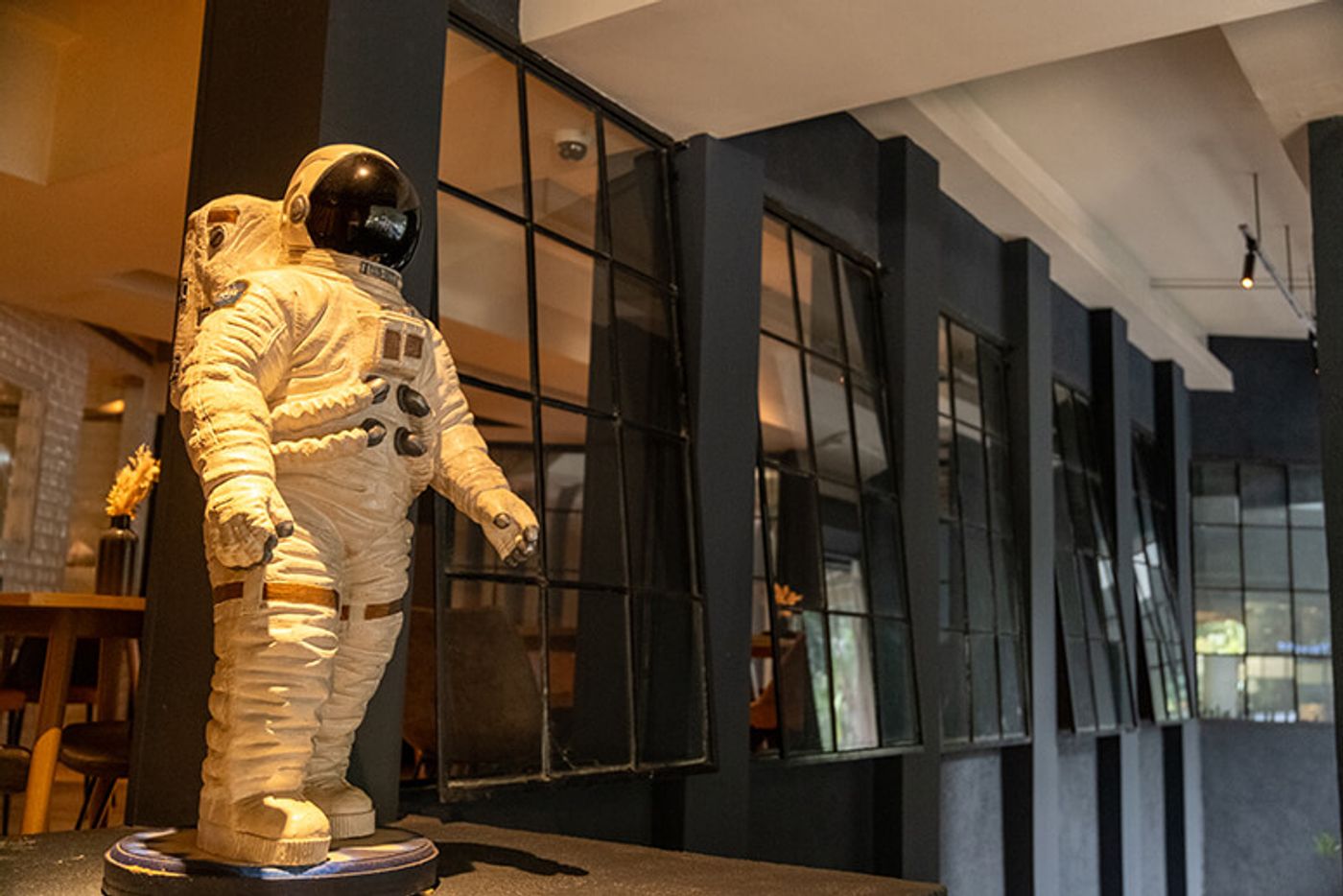White astronaut figure standing before black steel-framed windows at The Test Kitchen at One Rockwell