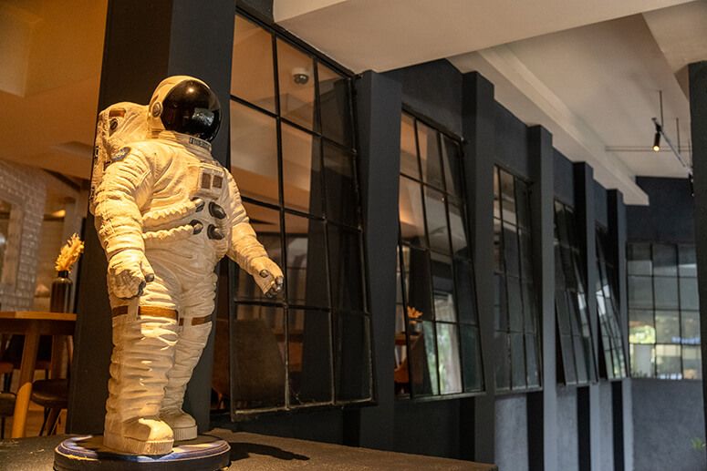 White astronaut figure standing before black steel-framed windows at The Test Kitchen at One Rockwell