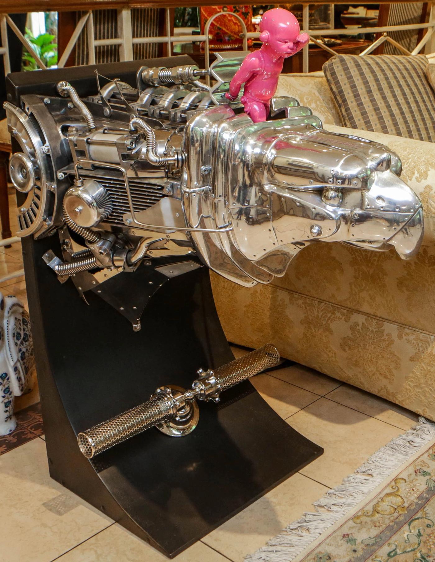 A chrome engine form with a pink infant figure astride it