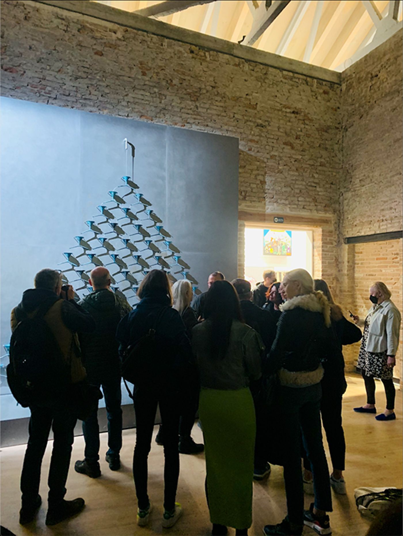 Visitors gather before Pavlo Makov’s pyramid of metal funnels on a wall in a brick-walled hall