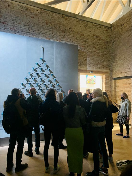 Visitors gather before Pavlo Makov’s pyramid of metal funnels on a wall in a brick-walled hall