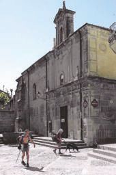 Two pilgrims crossing a sunlit square past a stone church in Santo Domingo de la Calzada