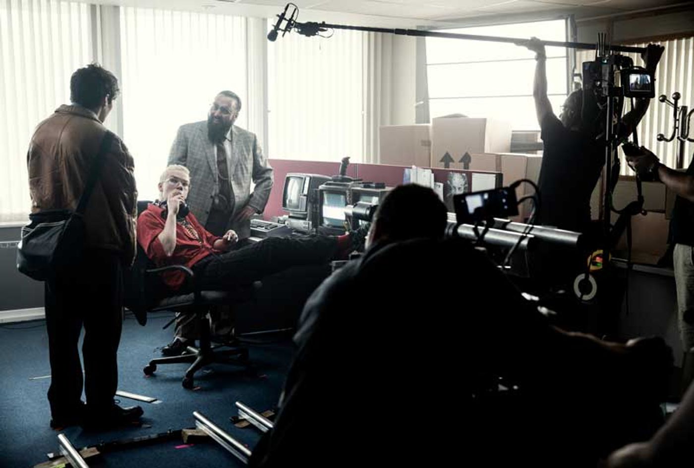 Film crew with boom mic and camera rig surround an actor in an office set during the Bandersnatch shoot