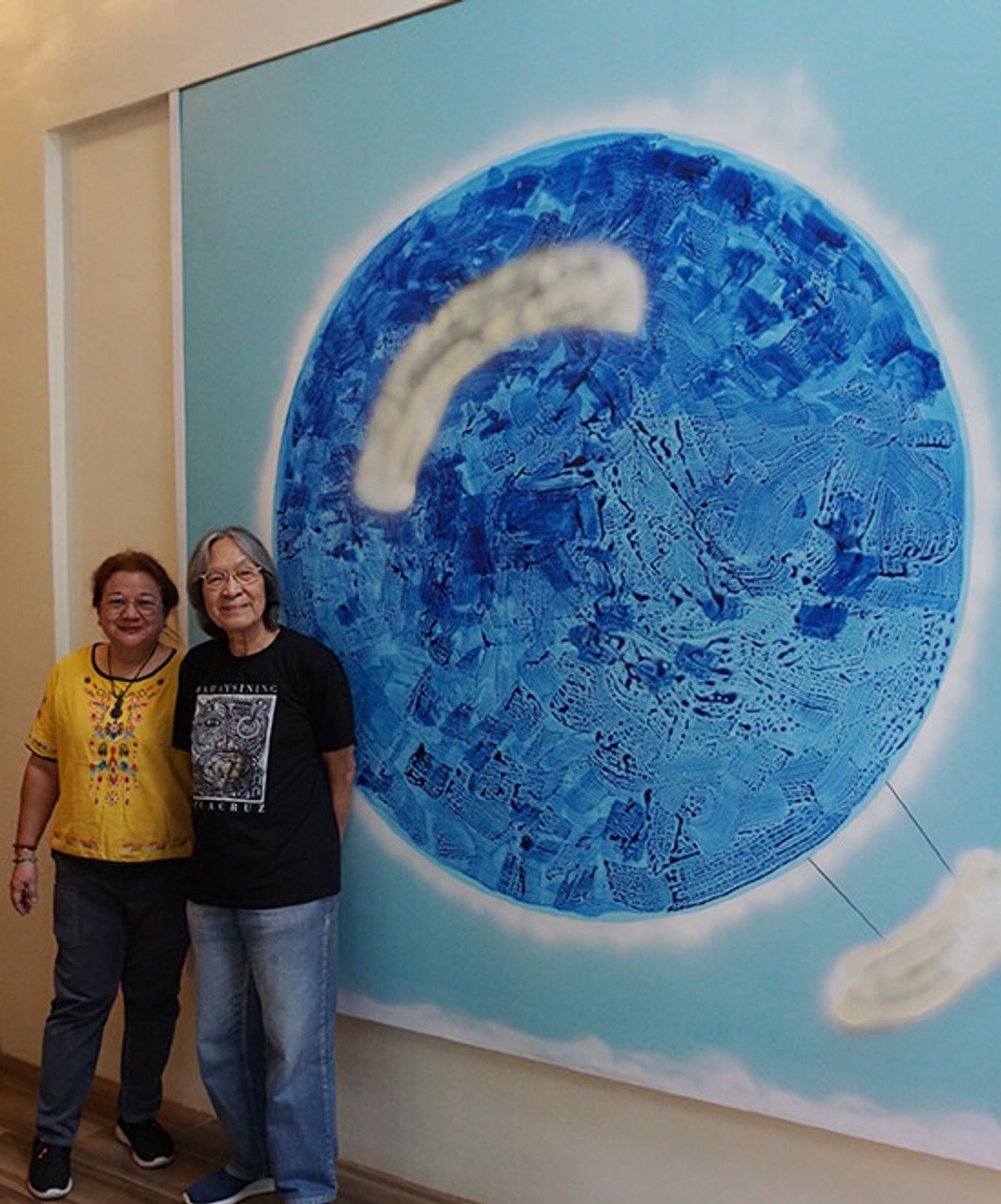 Tess and a companion standing before a wall-sized painting of a textured blue sphere in clouds