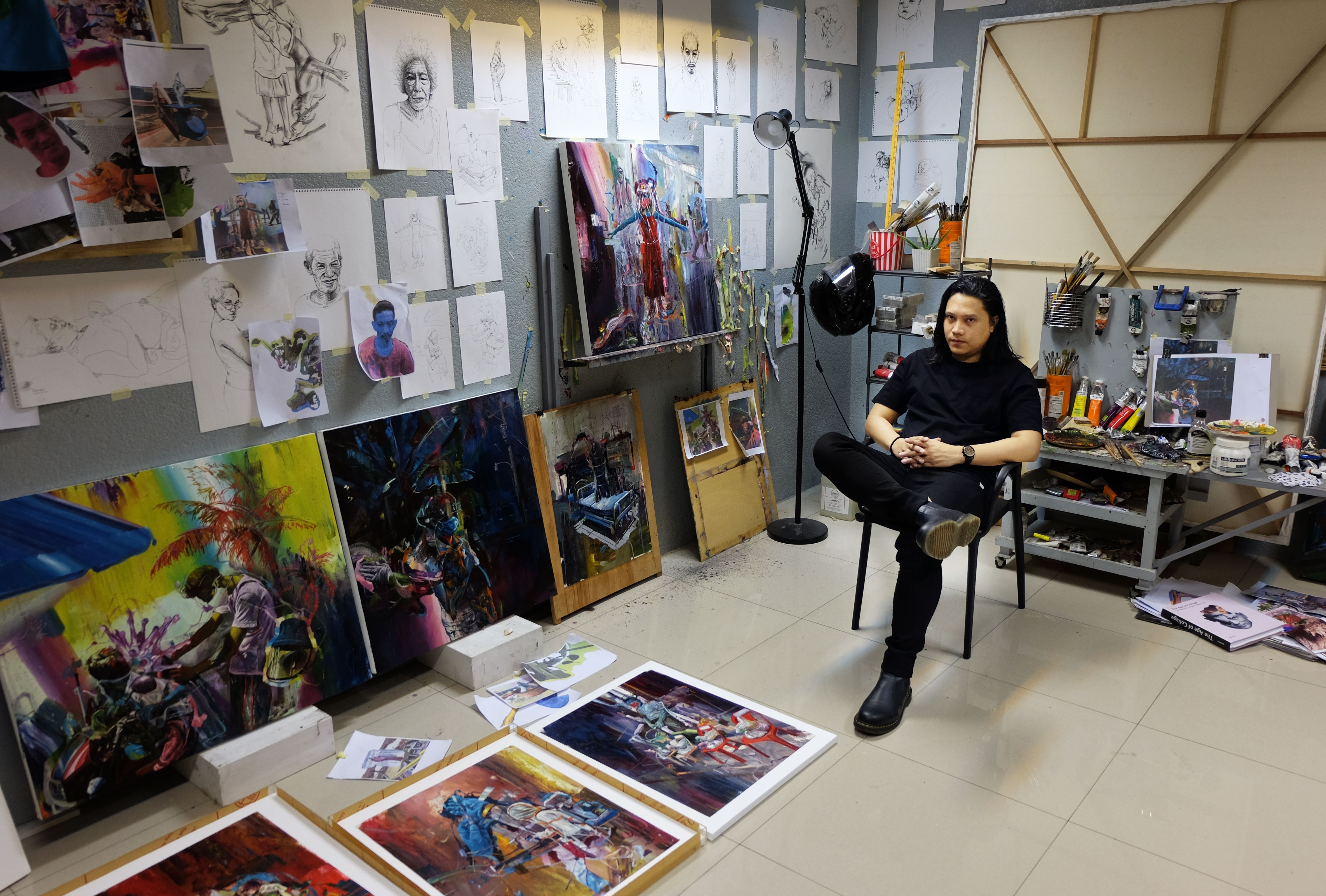 Ronson Culibrina sits in his studio surrounded by sketches, brushes and vivid canvases