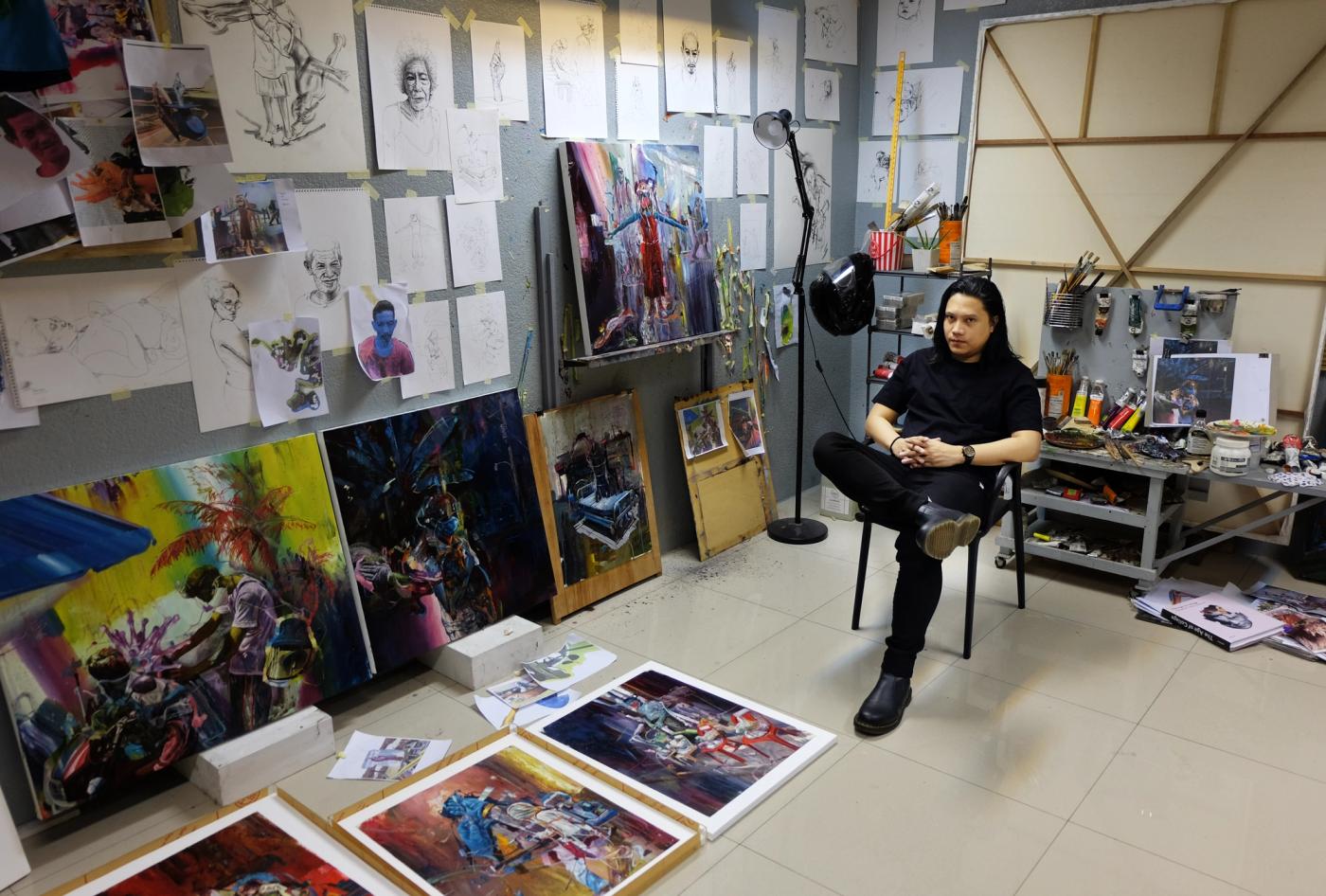 Ronson Culibrina sits in his studio surrounded by sketches, brushes and vivid canvases