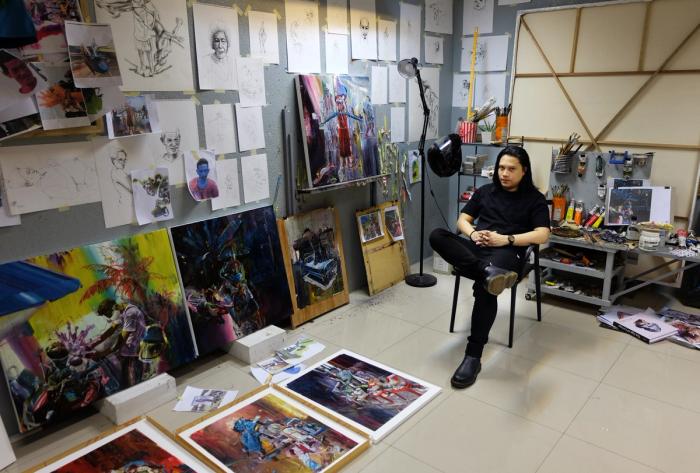 Ronson Culibrina sits in his studio surrounded by sketches, brushes and vivid canvases