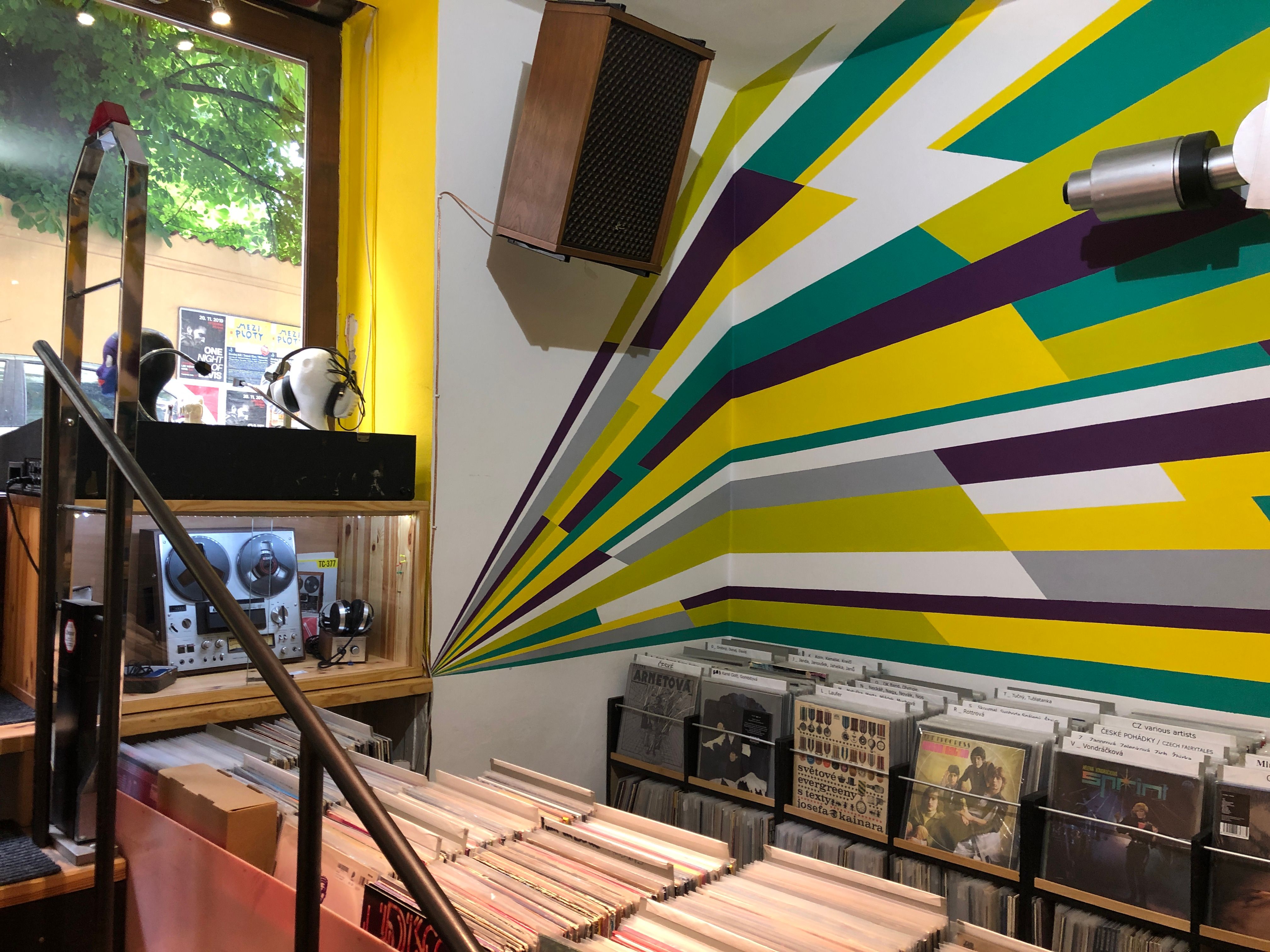 Record bins and headphones beneath a wall mural of green, yellow and purple rays