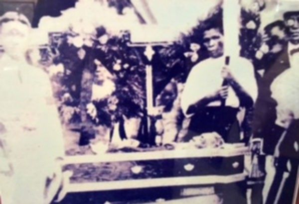 Faded photograph of a wake in Culion Island, Palawan: a flower-banked coffin beneath a crucifix, mourners standing on either side, one holding a candle