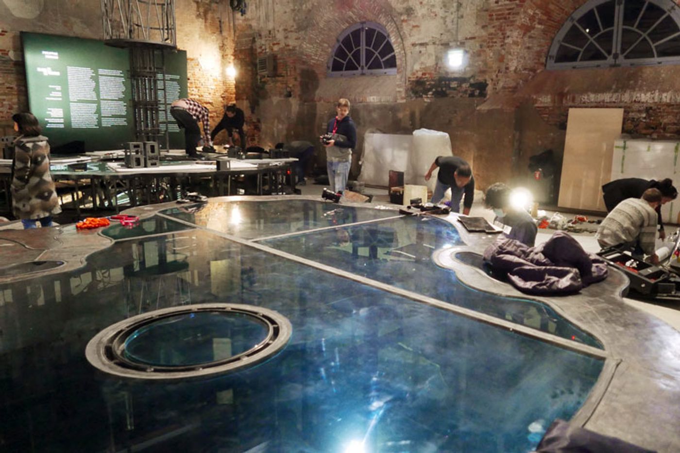 Crew dismantling Mark Justiniani’s Island Weather inside the Arsenale, its mirrored glass islands still reflecting the brick vaults