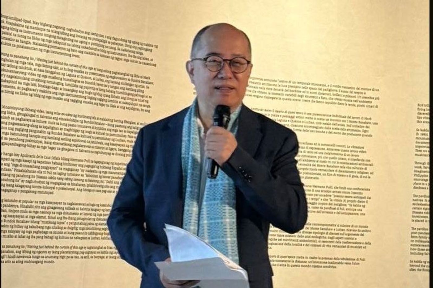 Philippine Pavilion commissioner Victorino “Ino” Manalo speaks at a microphone before a wall of exhibition text