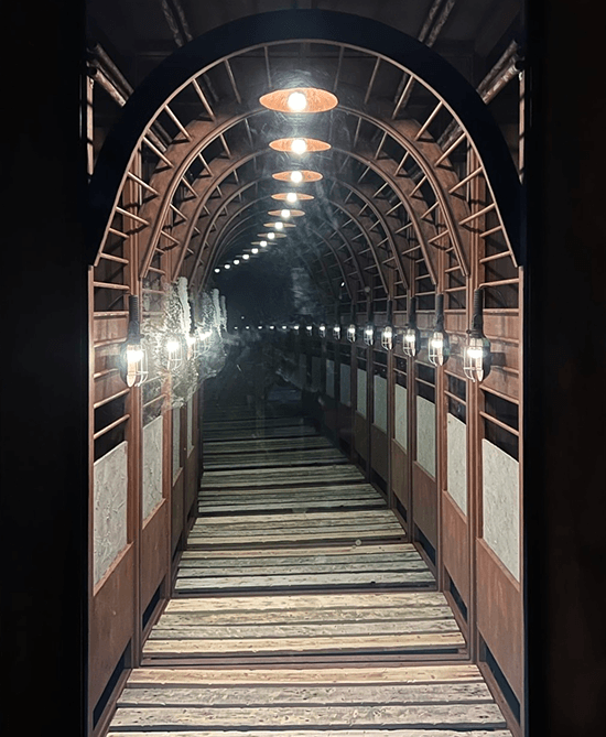 Mirrored installation of an arched wooden tunnel with lamps receding into infinite depth