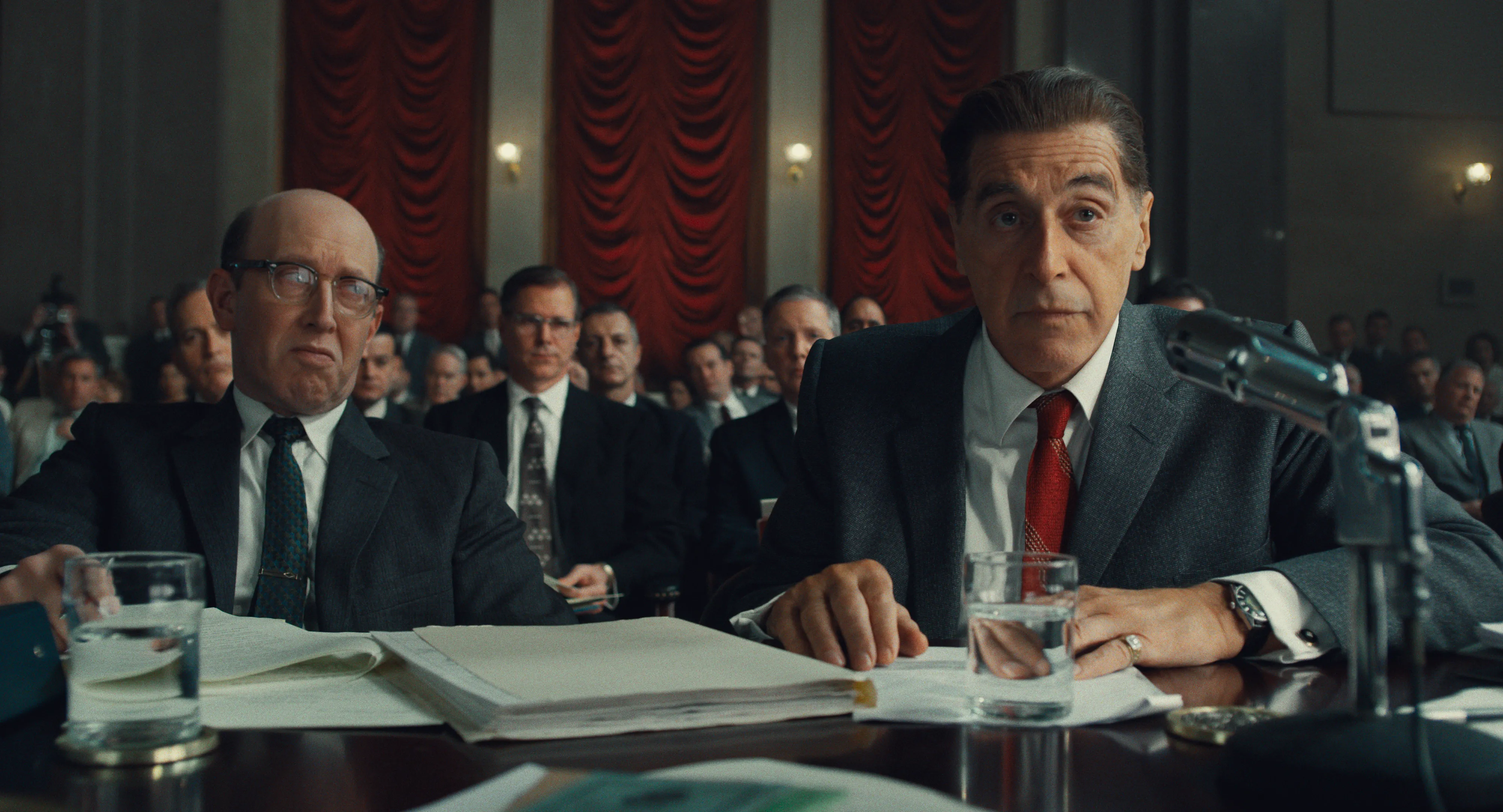 Al Pacino as Jimmy Hoffa speaks into microphones at a crowded Senate hearing in The Irishman