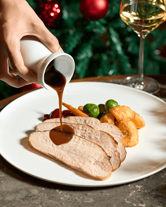 Gravy poured over sliced roast turkey breast with Brussels sprouts and roasted potatoes