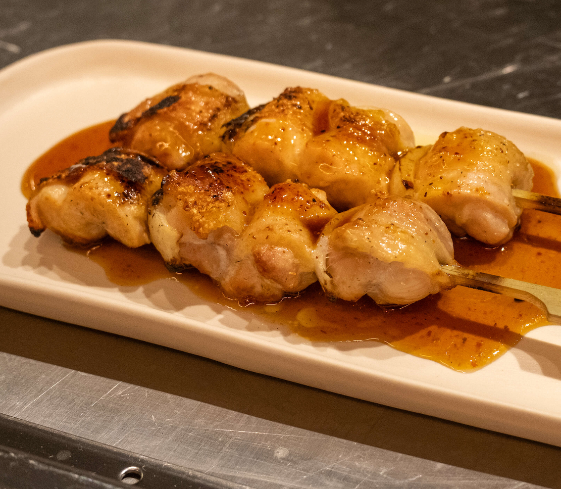 Glazed grilled chicken thigh skewers resting in their juices on a white plate