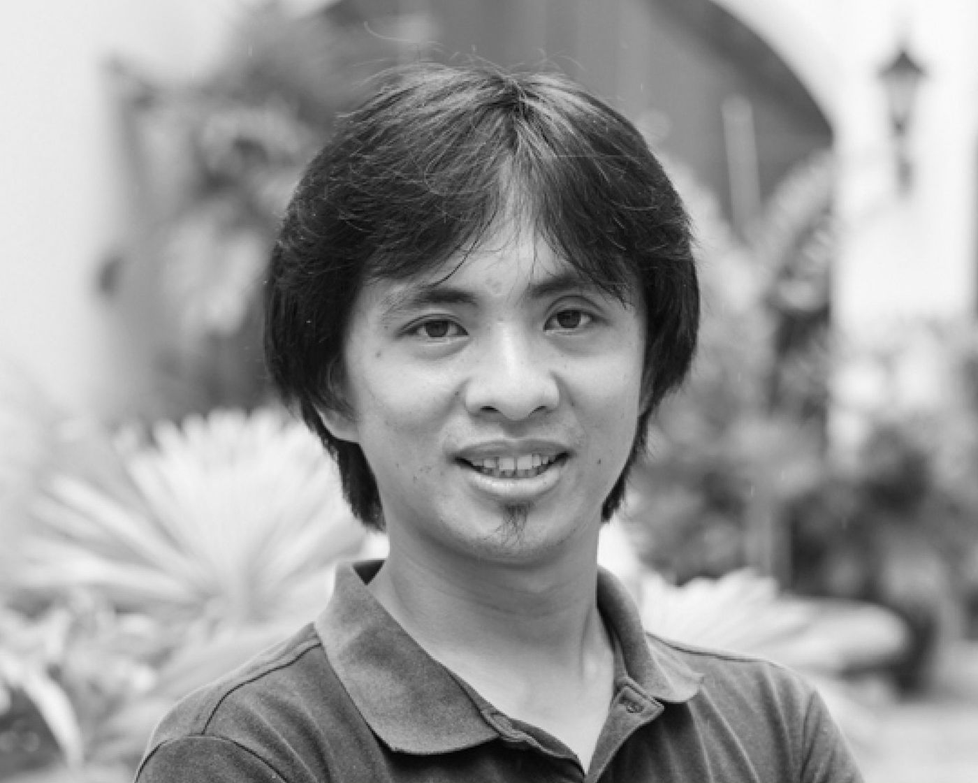 Black-and-white portrait of Sammy Buhle, smiling in a polo shirt amid garden foliage