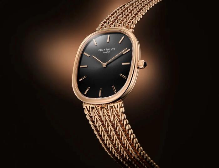 A rose-gold Patek Philippe Golden Ellipse watch with a black dial on a woven gold bracelet against a dark background