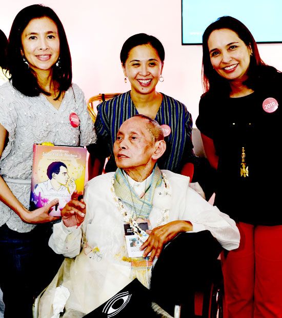 The three founders of Art Fair Philippines gathered around David Medalla in his wheelchair, one holding a book on Jaime Gil de Biedma
