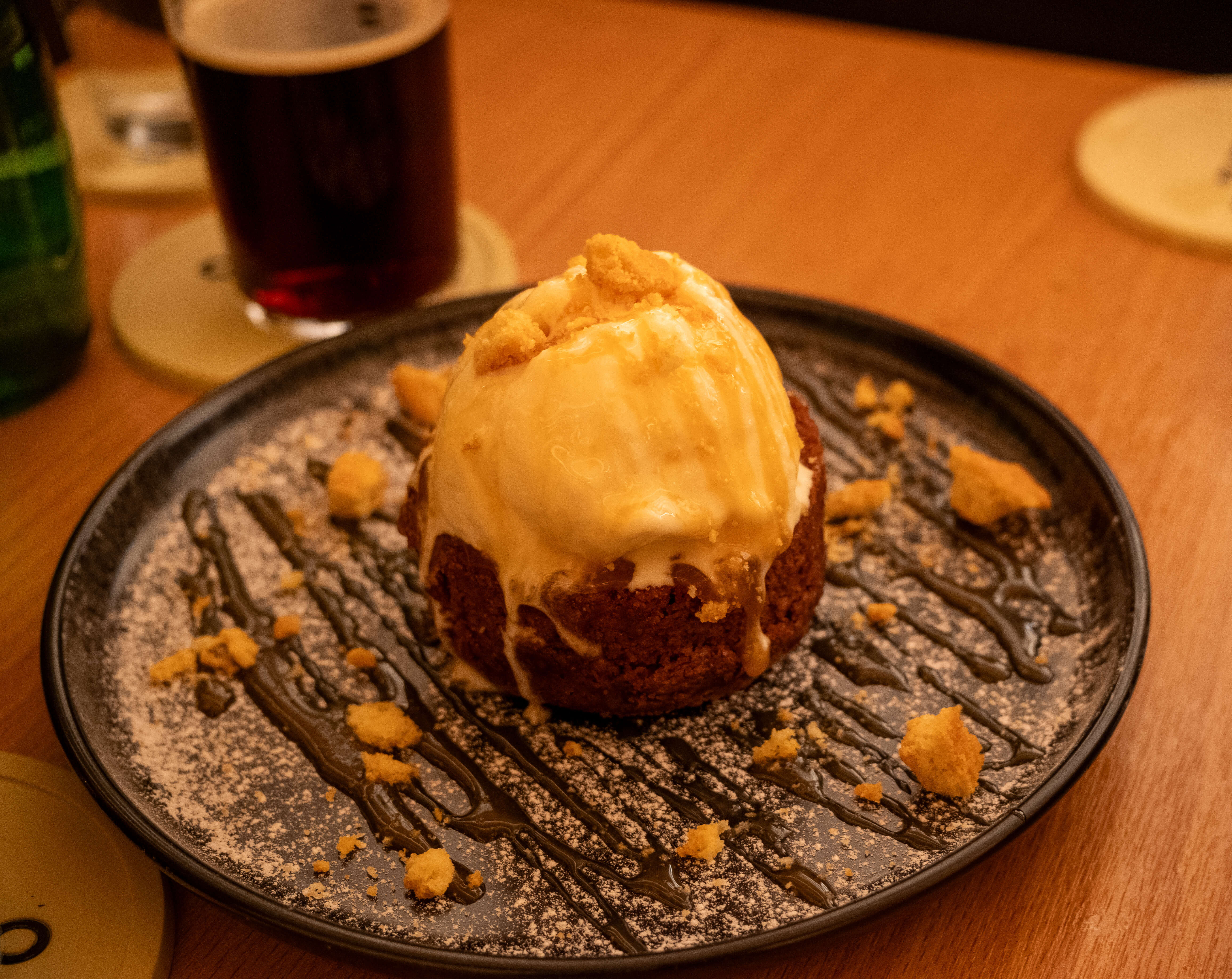 A warm dessert cake under a melting scoop of ice cream, chocolate drizzle and cookie crumble on a dark plate at Ippudo