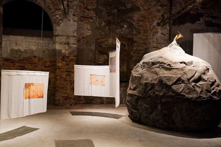 Installation inside the Philippine Pavilion at the Venice Biennale featuring a large grey boulder with a brass horn sticking out and hanging white textile sheets