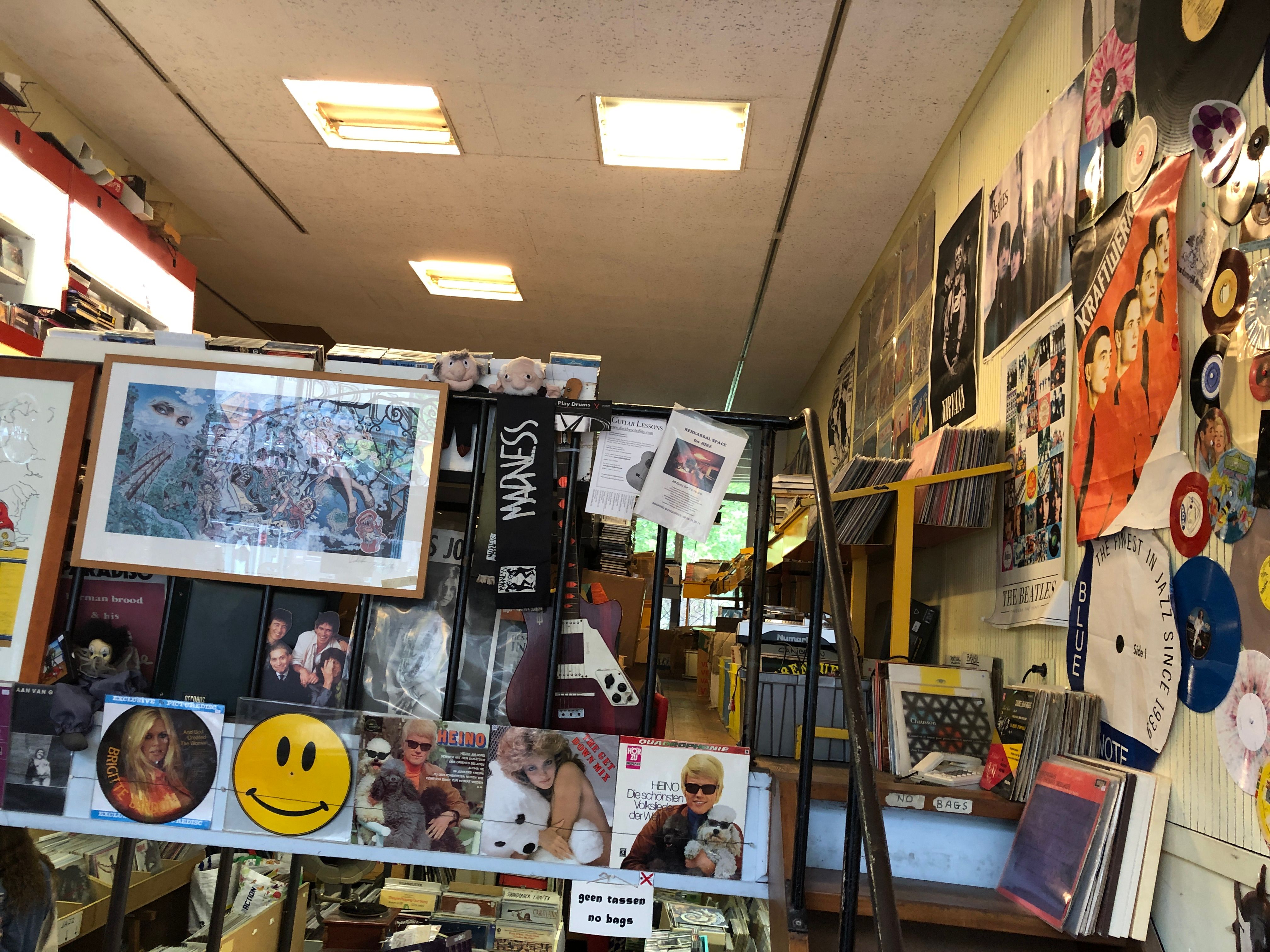 Cluttered record shop counter with a smiley-face disc, framed prints and stacked memorabilia