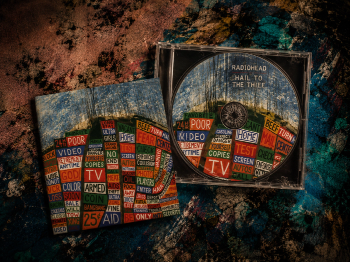 Radiohead’s Hail to the Thief CD and its road-sign collage sleeve lie open on a mottled, paint-splashed surface