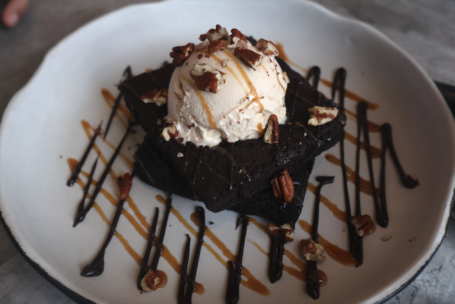 Chocolate brownie topped with vanilla ice cream, pecans and drizzles of caramel and fudge