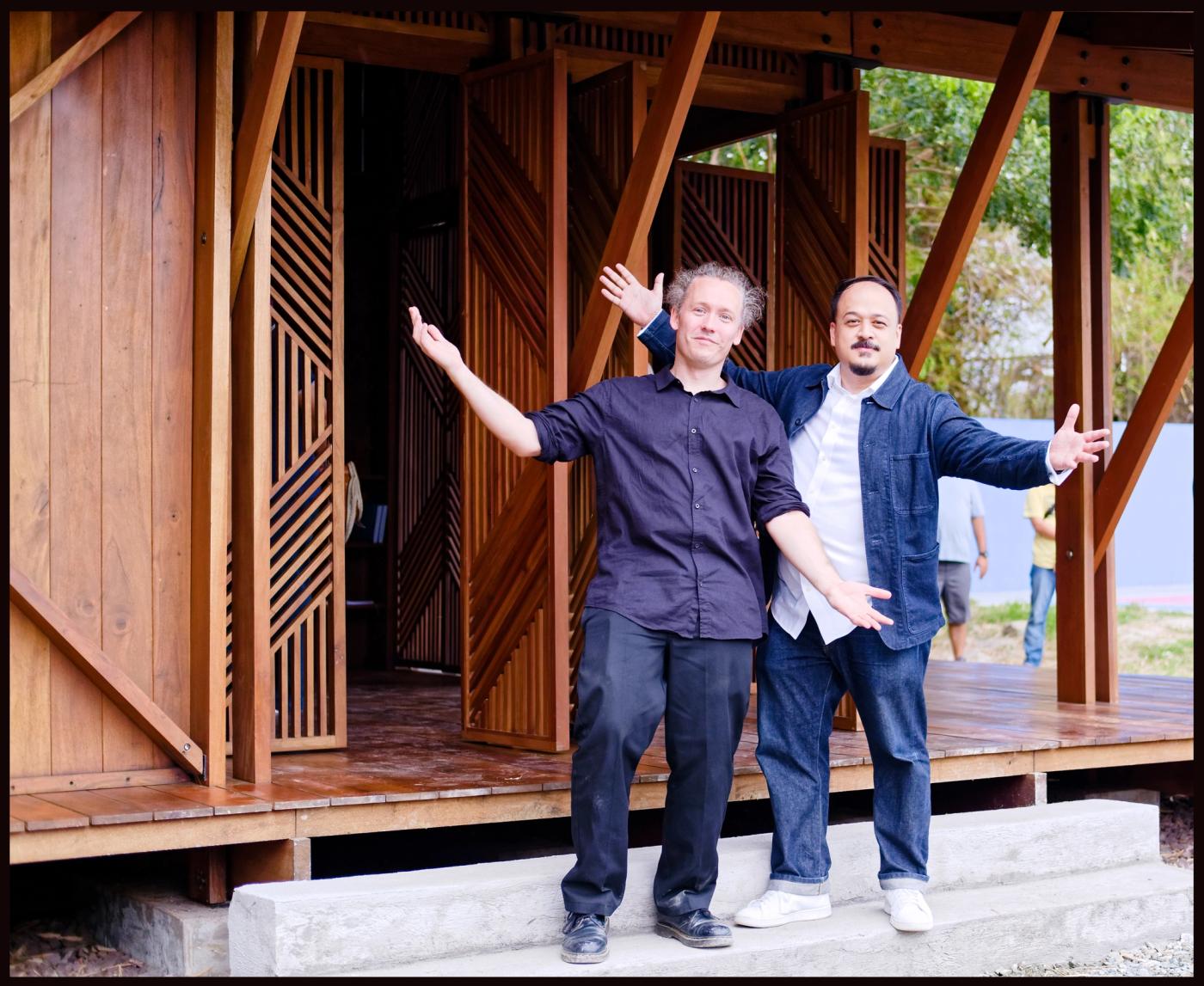 The ‘Structures of Mutual Support’ curators stand with arms outstretched before the pavilion’s wooden slatted library structure